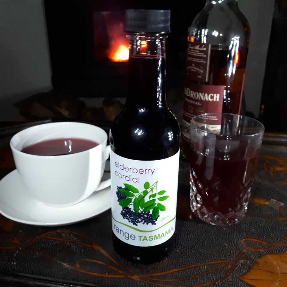 a cup of range Tasmania hot toddy with chamomile tea and elderberry cordial with a glass of whiskey on the side